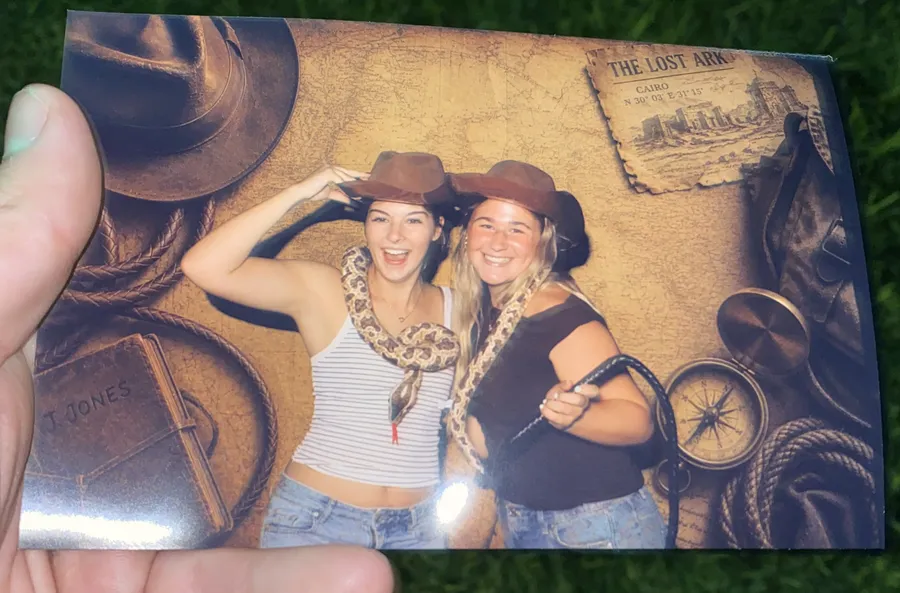 A print from the same event: two guests in cowboy hats with a snake on an adventure-map backdrop