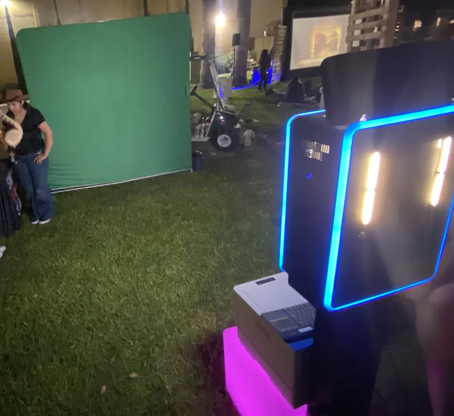 The booth setup at the same event: a green screen backdrop and a lit booth with its printer, on a lawn at night
